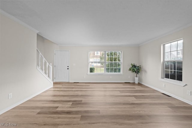 unfurnished living room featuring a wealth of natural light, light wood-style flooring, crown molding, and stairs