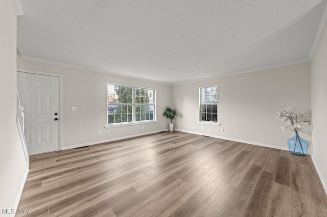 unfurnished living room featuring a textured ceiling, wood finished floors, baseboards, and ornamental molding