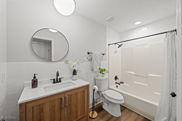 bathroom with toilet, vanity, shower / tub combo, wood finished floors, and tile walls