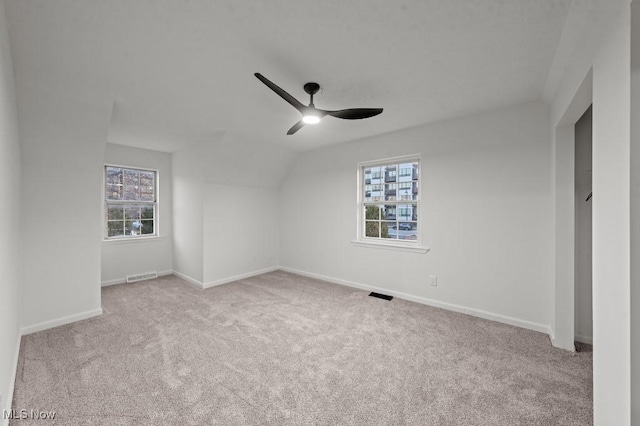 carpeted empty room with a ceiling fan, visible vents, and a wealth of natural light