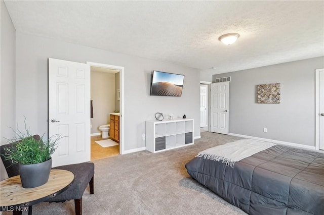 carpeted bedroom with ensuite bath, visible vents, a textured ceiling, and baseboards