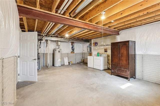 unfinished below grade area featuring water heater, brick wall, electric panel, and washing machine and clothes dryer