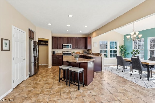 kitchen with a kitchen island, a breakfast bar, an inviting chandelier, stainless steel appliances, and dark brown cabinets