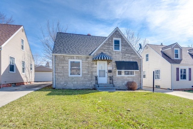 view of front facade with stone siding, an outbuilding, a front lawn, and a shingled roof