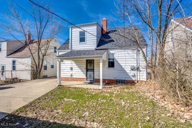 exterior space featuring concrete driveway, a front yard, roof with shingles, and a chimney