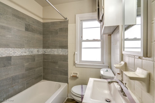 bathroom with washtub / shower combination, toilet, tile walls, and a sink