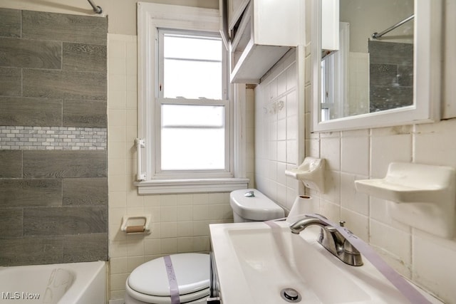 bathroom featuring a sink, shower / bathing tub combination, toilet, and tile walls