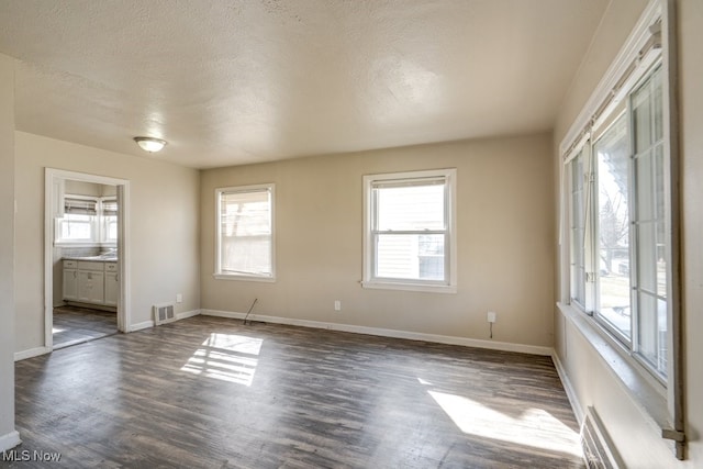 spare room featuring visible vents, baseboards, a textured ceiling, and dark wood finished floors