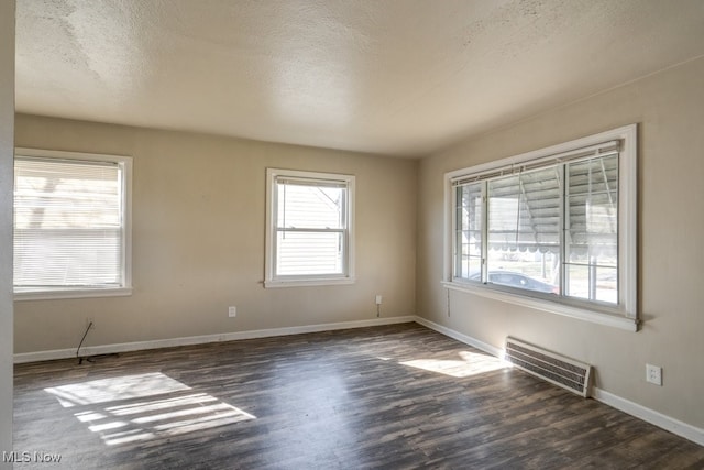 empty room with visible vents, baseboards, a textured ceiling, and dark wood-style floors