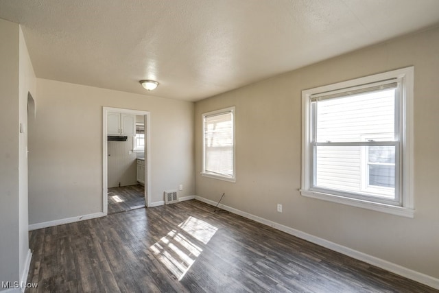 unfurnished bedroom with dark wood finished floors, baseboards, visible vents, and a textured ceiling