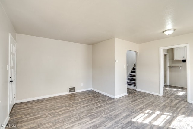 unfurnished room with visible vents, baseboards, stairs, wood finished floors, and arched walkways