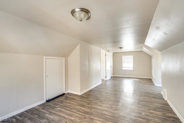 additional living space with baseboards, dark wood finished floors, and vaulted ceiling