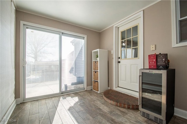 doorway to outside with crown molding, baseboards, wood tiled floor, beverage cooler, and a dry bar