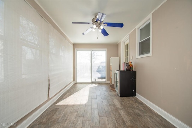 empty room with a ceiling fan, dark wood-style floors, baseboards, and ornamental molding