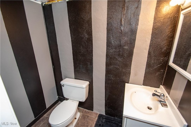 half bathroom with vanity, tile patterned floors, toilet, and a textured wall