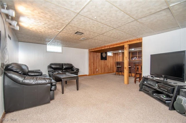 carpeted living room with a paneled ceiling, baseboards, and wood walls