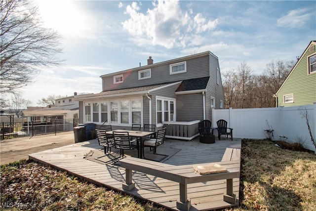 rear view of house with a deck, a fenced backyard, a chimney, and a shingled roof