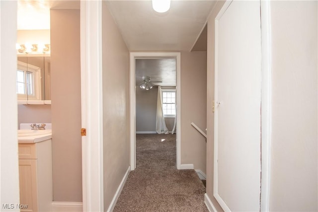 hallway with carpet, baseboards, and a sink