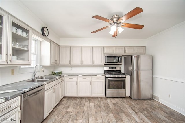 kitchen featuring light wood-style flooring, ornamental molding, a sink, appliances with stainless steel finishes, and ceiling fan