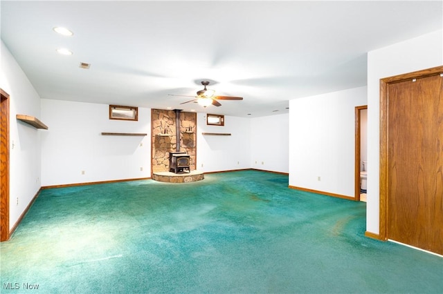 unfurnished living room with visible vents, baseboards, carpet floors, a wood stove, and ceiling fan