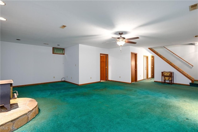 unfurnished living room with carpet, a wood stove, a ceiling fan, and baseboards