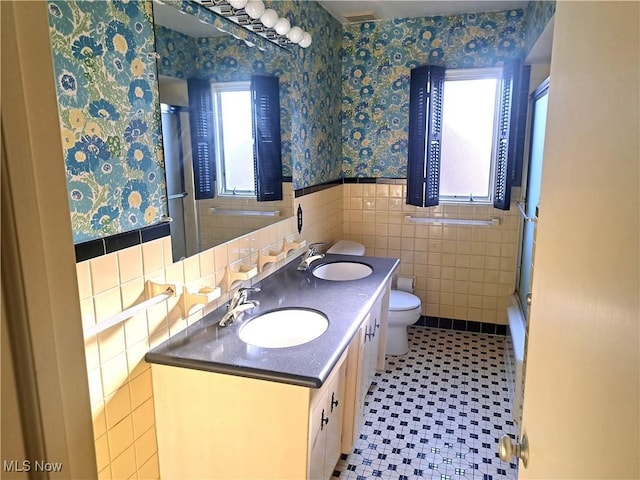 bathroom featuring an enclosed shower, wainscoting, wallpapered walls, and a sink