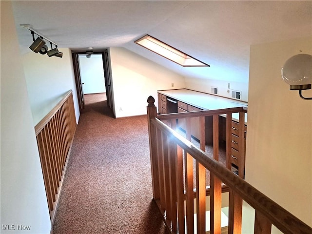 hall with rail lighting, vaulted ceiling with skylight, carpet flooring, and an upstairs landing