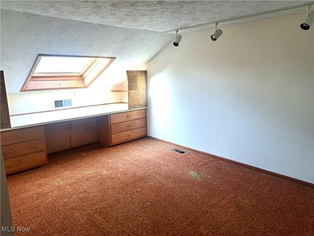 additional living space with lofted ceiling with skylight, visible vents, light colored carpet, and built in study area