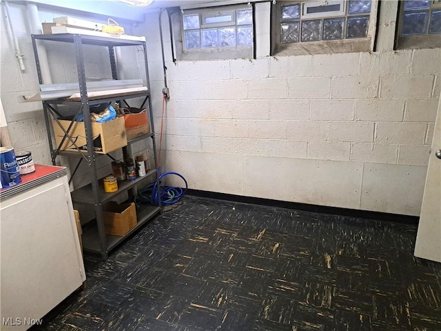 below grade area with tile patterned floors, concrete block wall, and fridge