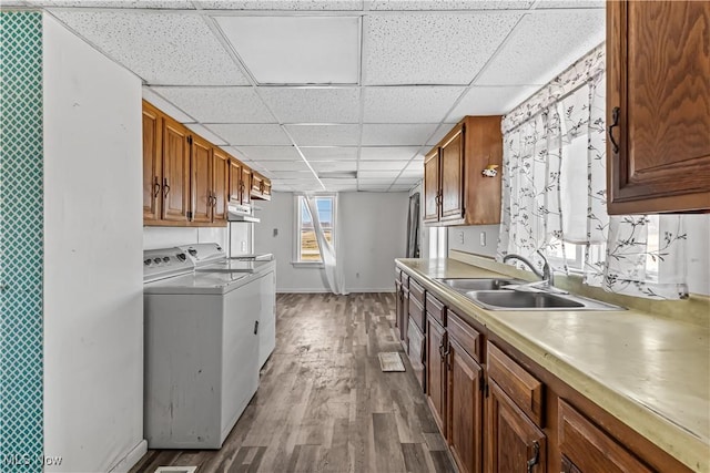 kitchen with a sink, independent washer and dryer, wood finished floors, and light countertops