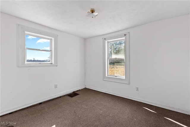 spare room featuring visible vents, dark carpet, and baseboards