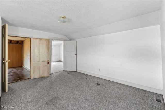 unfurnished bedroom featuring visible vents, light carpet, lofted ceiling, a textured ceiling, and baseboards