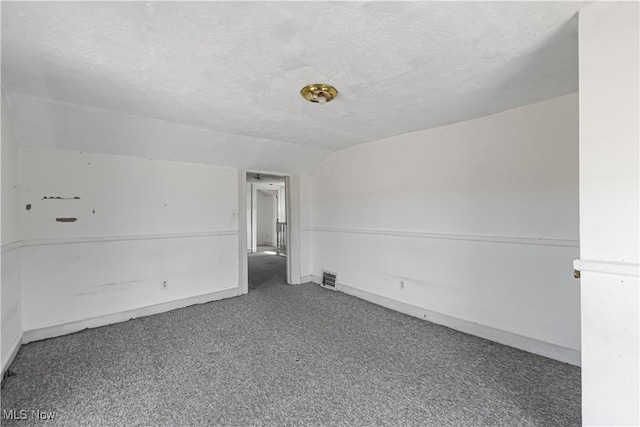 unfurnished room featuring carpet flooring, a textured ceiling, visible vents, and vaulted ceiling