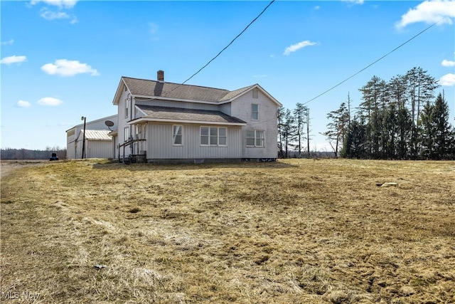 rear view of house featuring roof with shingles and a chimney