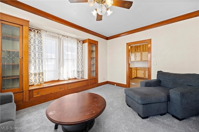 carpeted living area featuring baseboards, ceiling fan, and crown molding