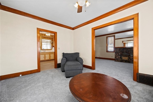 sitting room featuring visible vents, ornamental molding, carpet, a stone fireplace, and baseboards