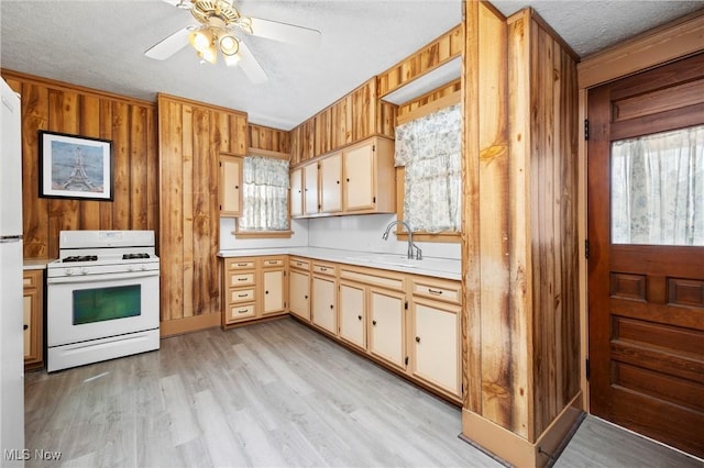 kitchen with light wood finished floors, white gas stove, wood walls, light countertops, and a sink