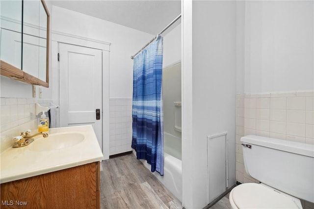 full bathroom with a wainscoted wall, toilet, wood finished floors, tile walls, and vanity