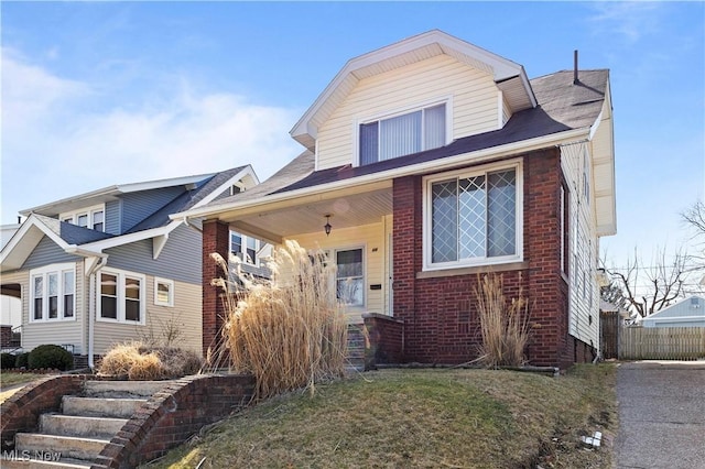 view of front facade with brick siding, a front lawn, and fence