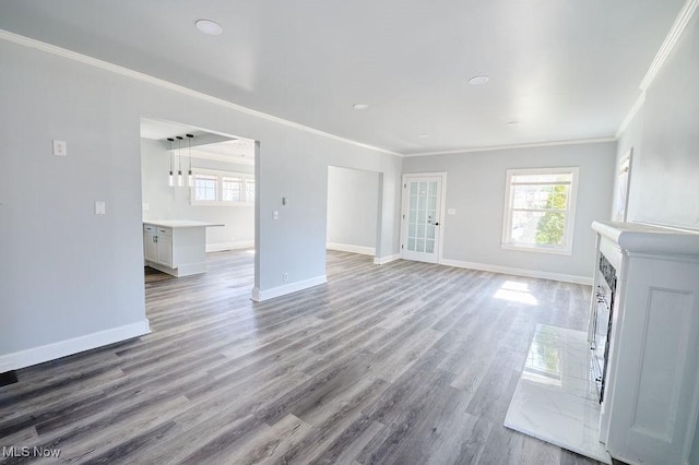 unfurnished living room with baseboards, light wood-style floors, ornamental molding, and plenty of natural light