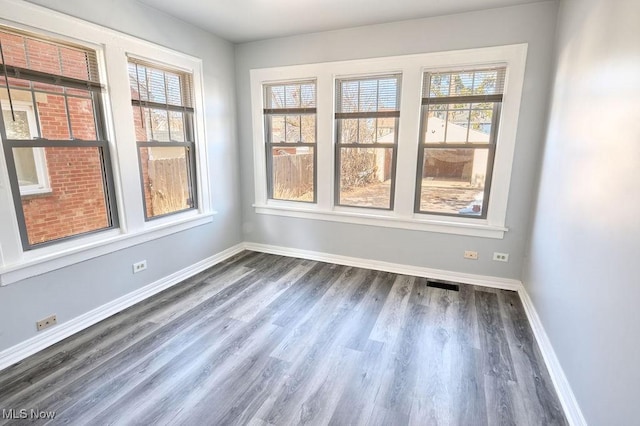 empty room featuring dark wood-type flooring, visible vents, and baseboards