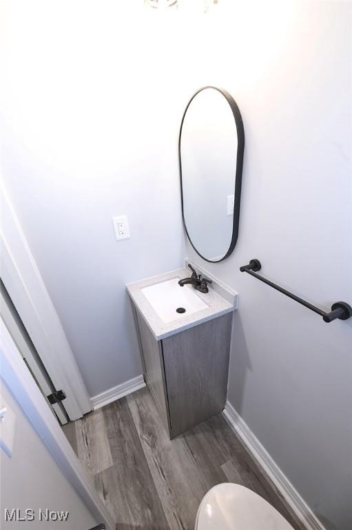 half bath featuring vanity, toilet, wood finished floors, and baseboards