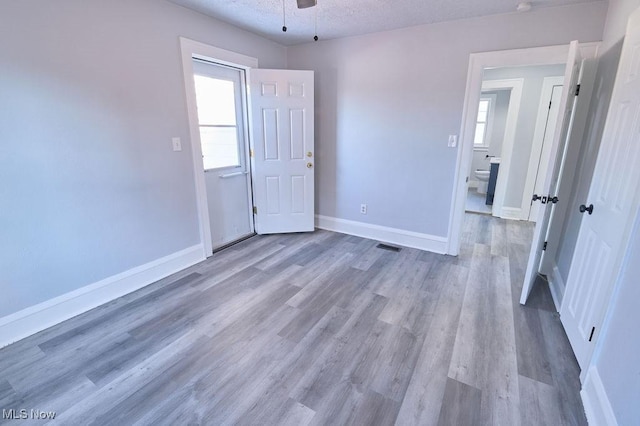 unfurnished bedroom with multiple windows, a textured ceiling, baseboards, and wood finished floors