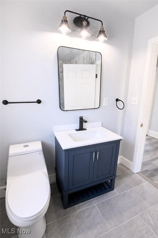 half bathroom featuring baseboards, toilet, and vanity