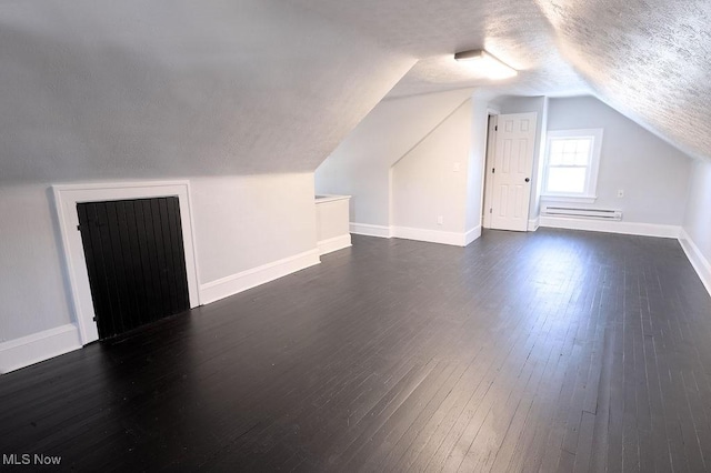 additional living space with baseboards, lofted ceiling, dark wood-style flooring, a textured ceiling, and a baseboard heating unit