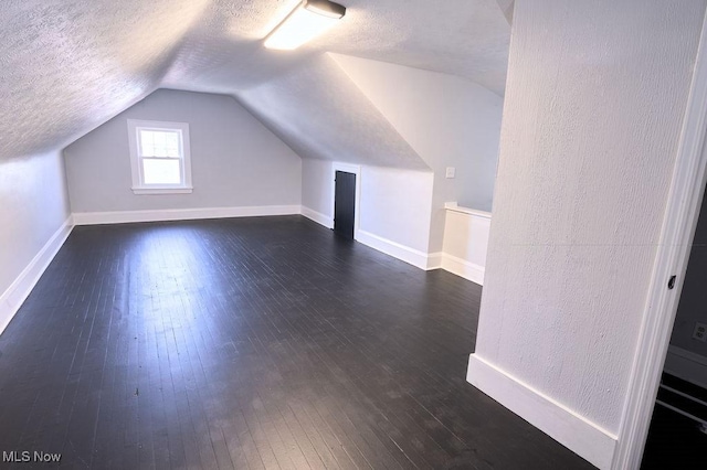 additional living space featuring lofted ceiling, a textured ceiling, and dark wood finished floors