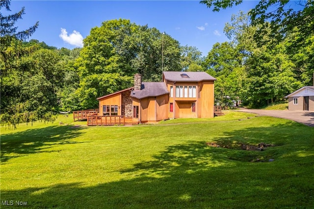 rear view of property featuring a lawn, a deck, and a chimney