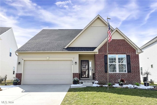 traditional home with driveway, roof with shingles, an attached garage, a front yard, and brick siding