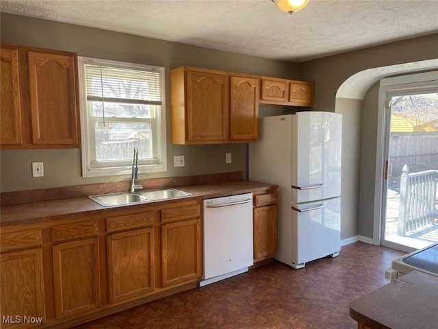 kitchen with dark floors, brown cabinets, white appliances, a textured ceiling, and a sink