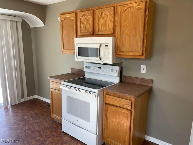 kitchen with baseboards, white appliances, dark countertops, and arched walkways